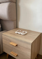 Plateau faro beige en jesmonite posé sur une petite commode en bois clair dans une chambre avec dessus des lunettes.