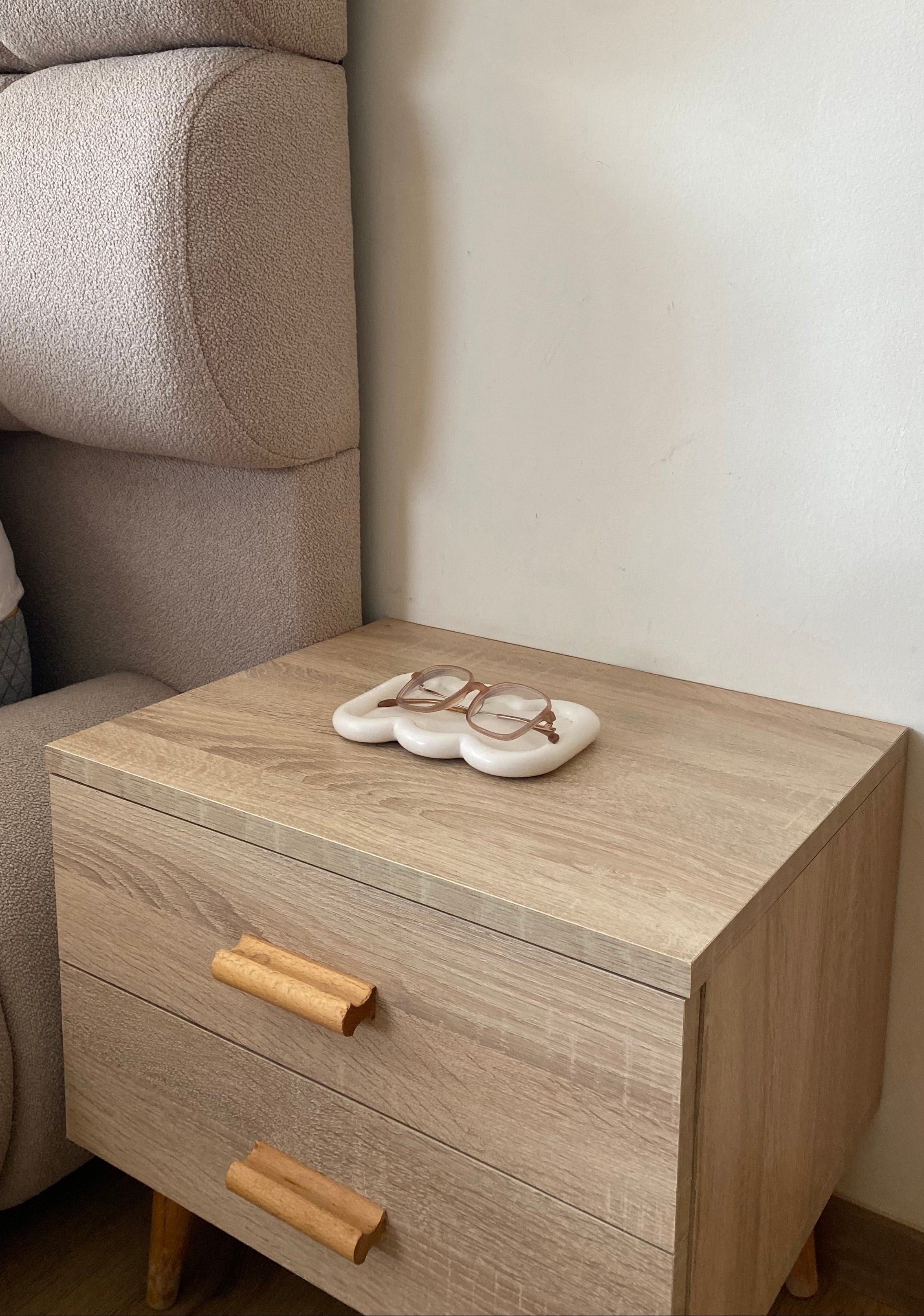 Plateau faro beige en jesmonite posé sur une petite commode en bois clair dans une chambre avec dessus des lunettes.