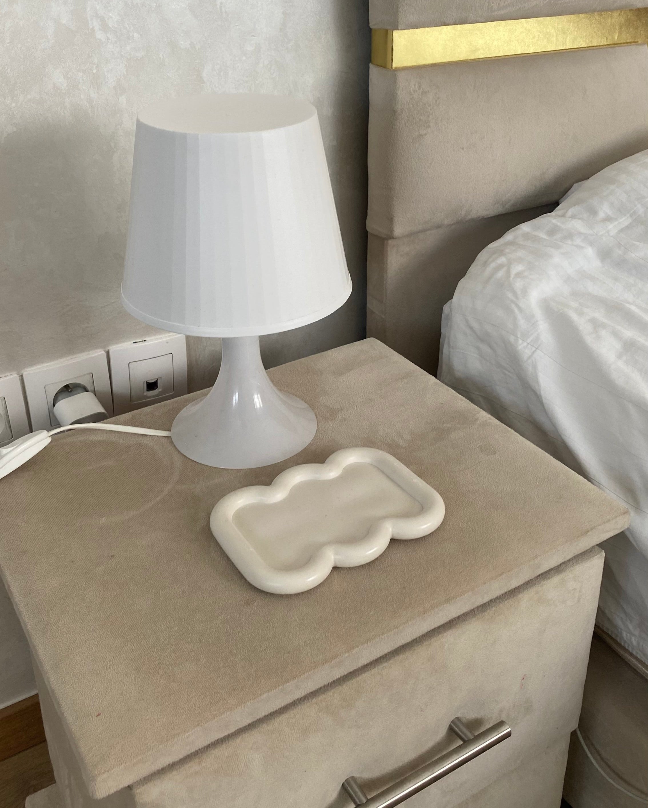 Plateau faro beige en jesmonite posé sur une petite commode en velour beige clair dans une chambre.