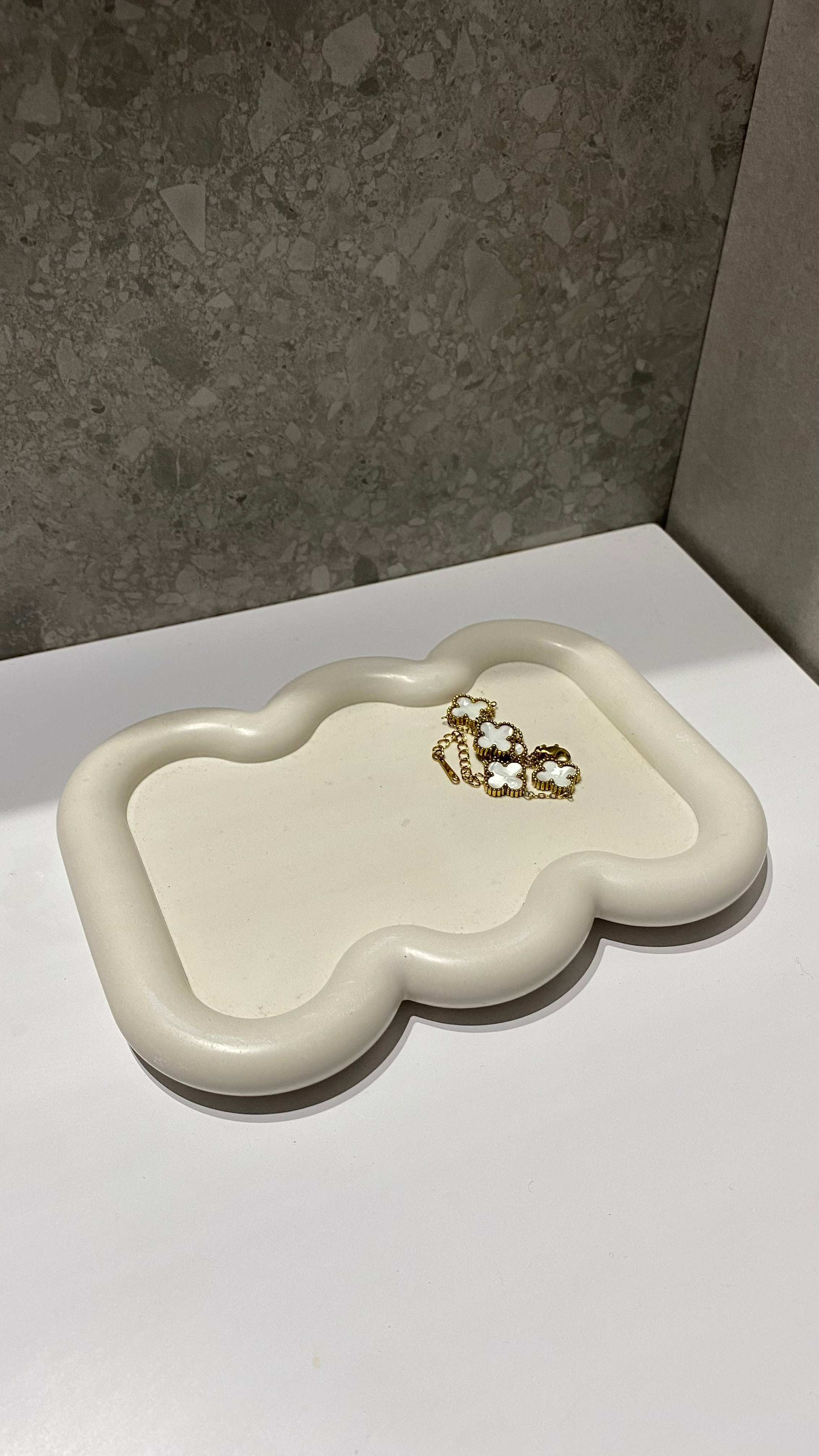 Plateau faro beige en jesmonite posé sur un évier dans une salle de bain avec dessus un bracelet.