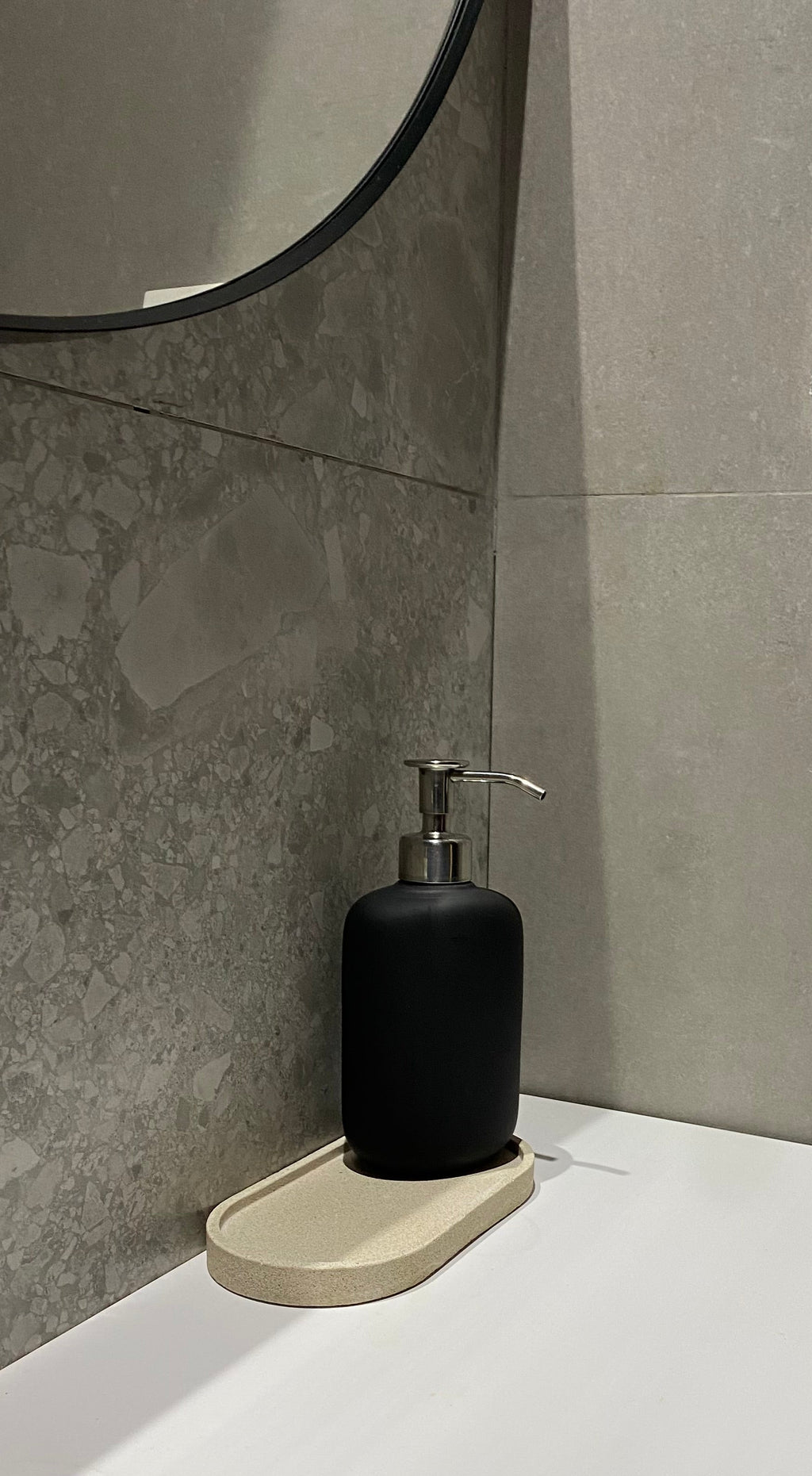 Plateau décoratif en jesmonite avec une forme ovale de couleur beige avec une texture pierre brute posé sur un lavabo.