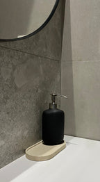 Plateau décoratif en jesmonite avec une forme ovale de couleur beige avec une texture pierre brute posé sur un lavabo.