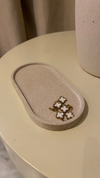 Plateau décoratif en jesmonite avec une forme ovale de couleur beige avec une texture pierre brute posé sur une table de chevet
